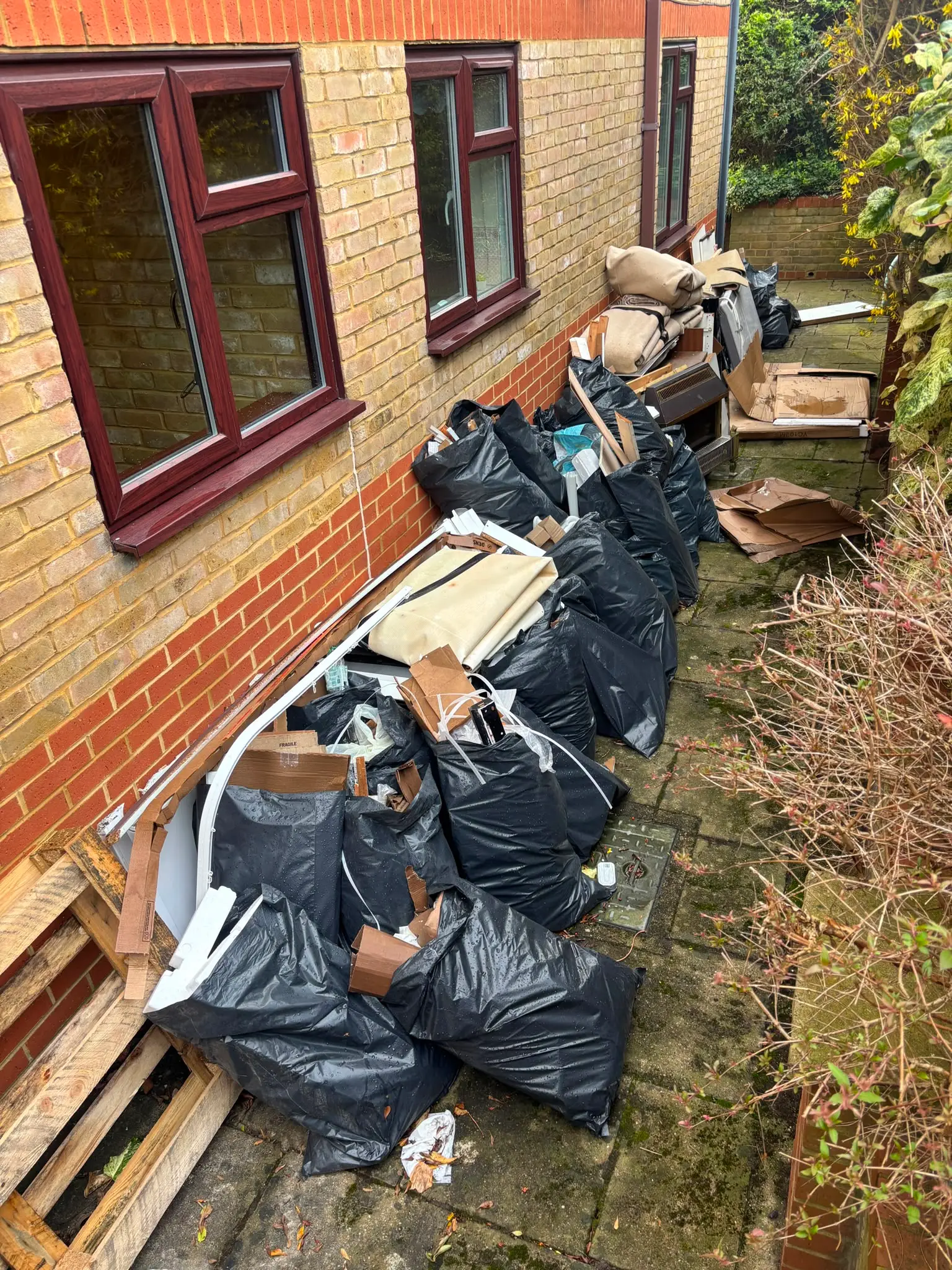 Bagged waste arranged along the side access of a residential property.