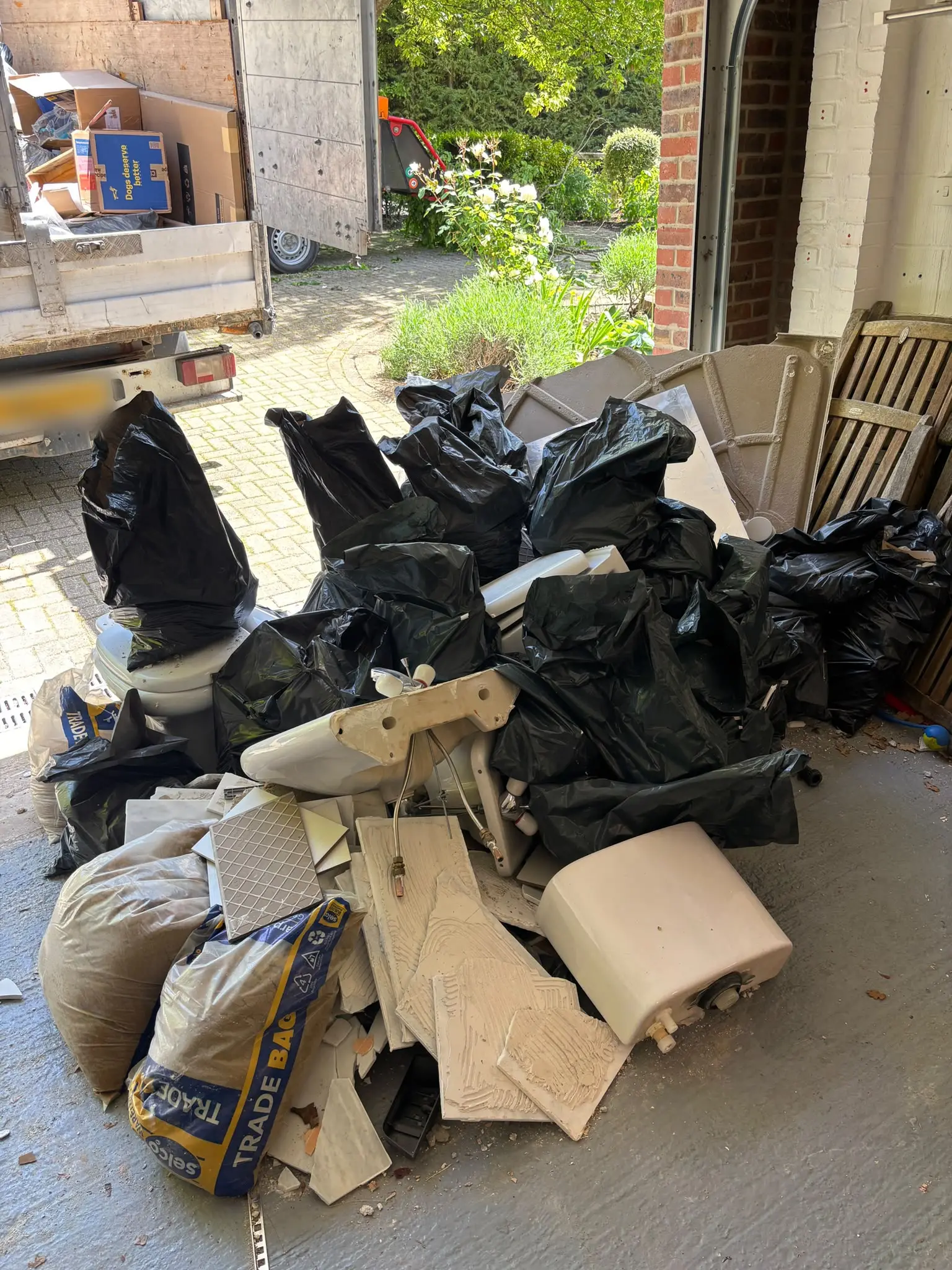 Old bath, basin, toilet, tiles and trade bags stacked in a garage doorway beside the tipper truck.