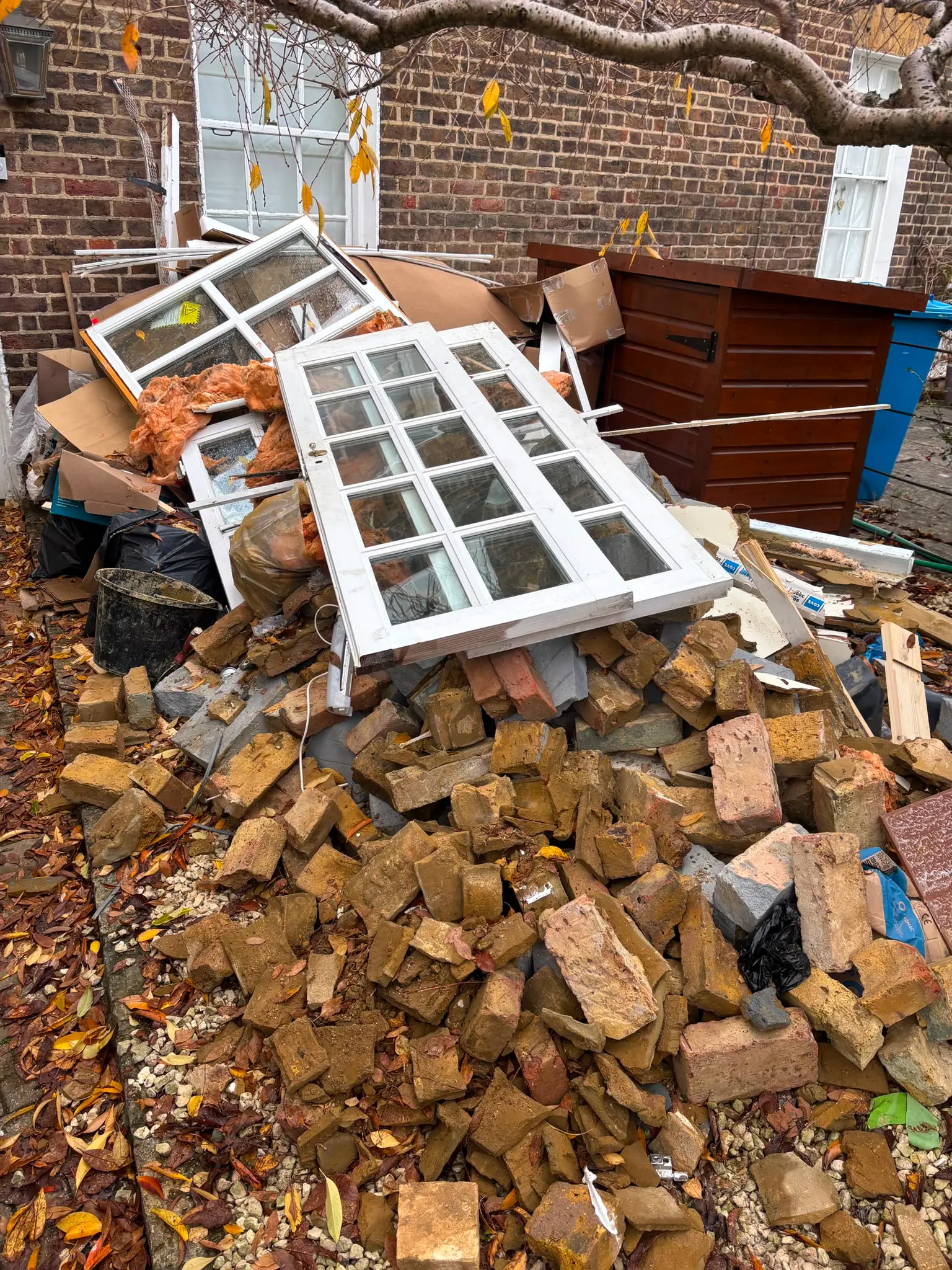 Old sash window frames, bricks, insulation and cardboard piled across a brick courtyard before clearance.