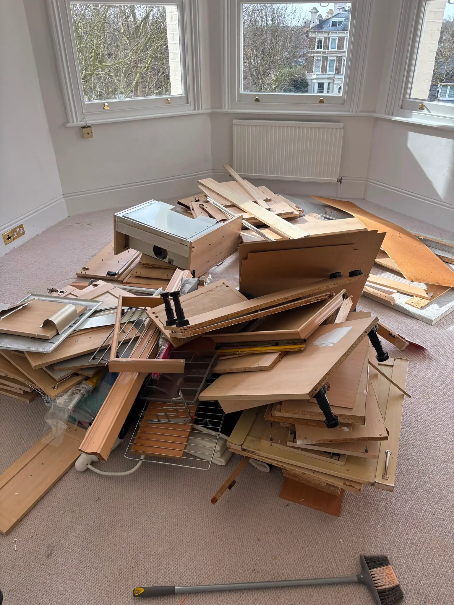 Dismantled wardrobes and flat-pack furniture stacked in a bay-window room ready for removal.