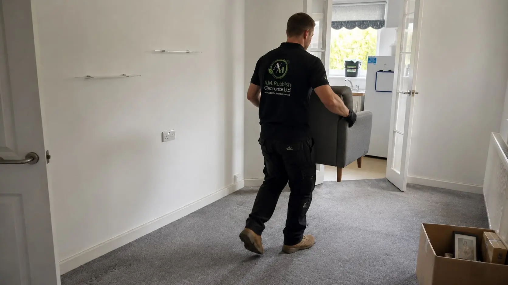Clearance worker carrying an armchair from a mostly cleared British rental property.
