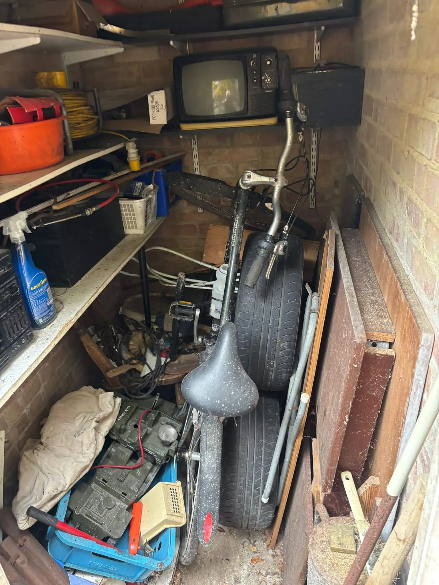 Small brick garage packed with a bicycle, tyres, old electronics and stored items before clearance.