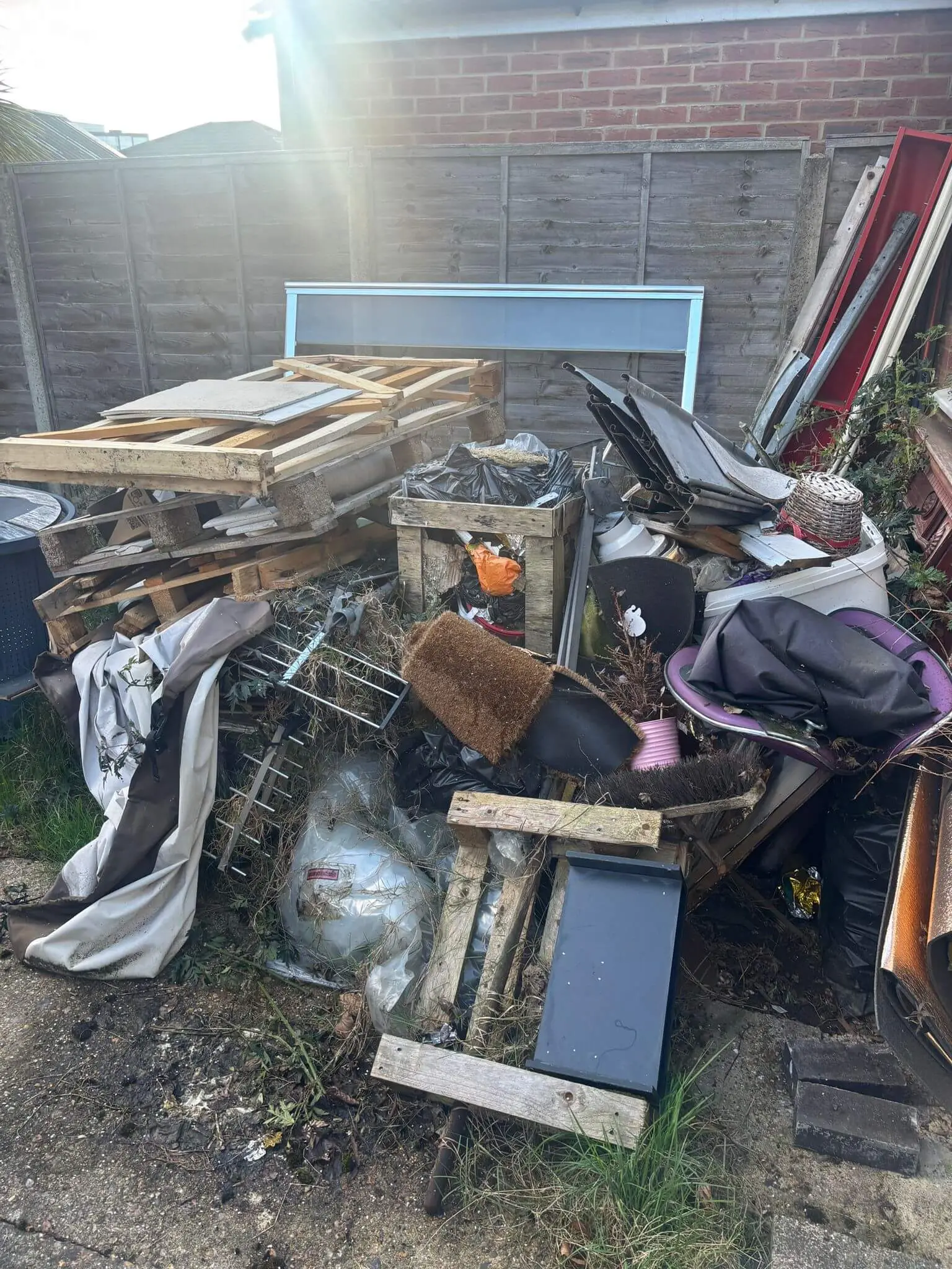 Garden corner filled with pallets, bags and mixed bulky waste before clearance.