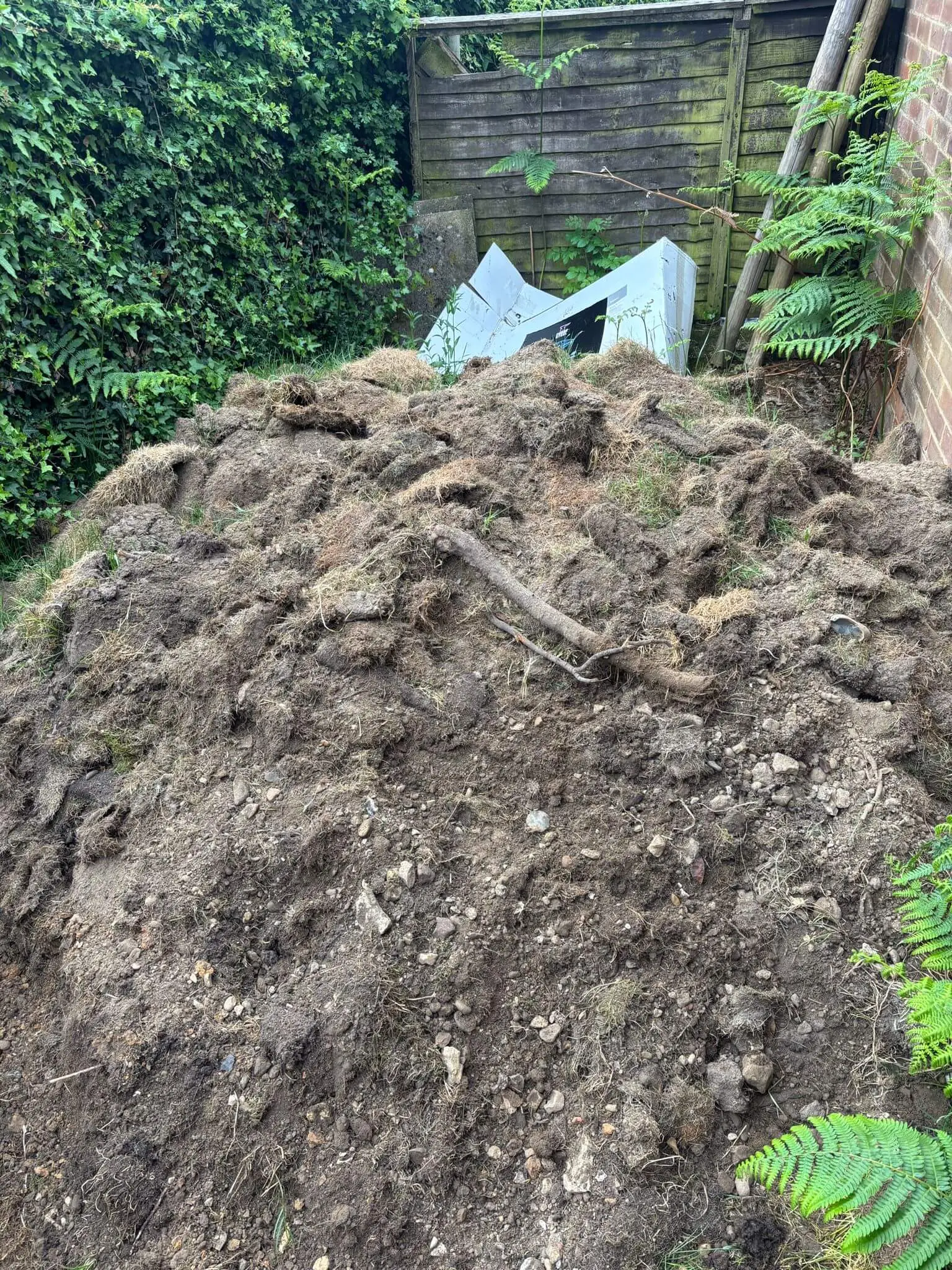 Large mound of soil, turf and garden excavation waste before removal.