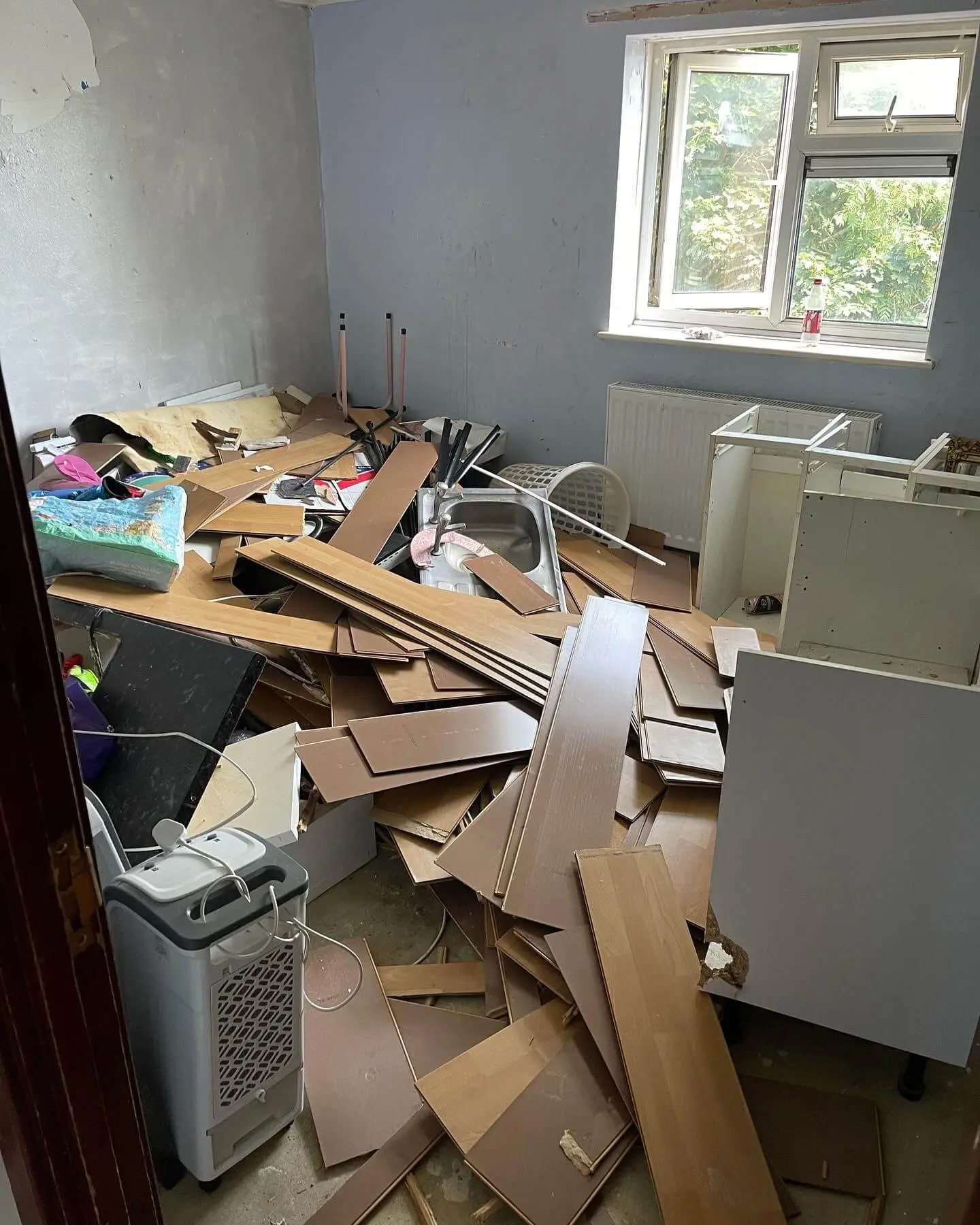 Residential room filled with dismantled units, flooring and refurbishment waste before clearance.