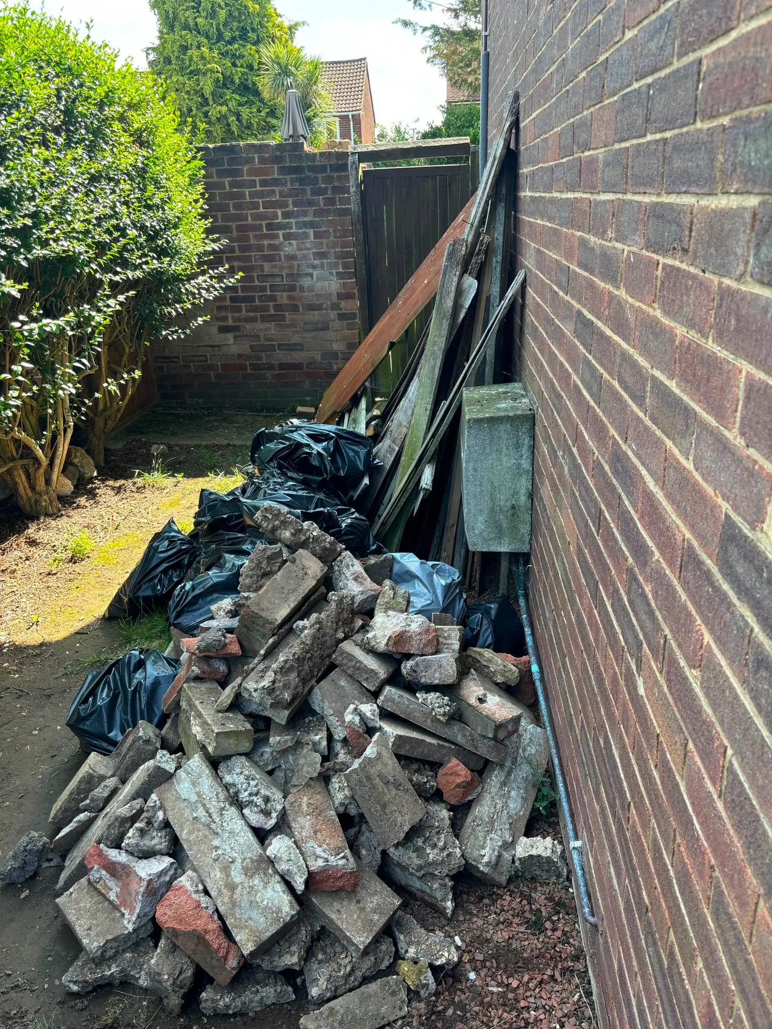 Rubble and broken brick in a garden Broken bricks and concrete piled against a house wall, with bagged waste and timber behind.