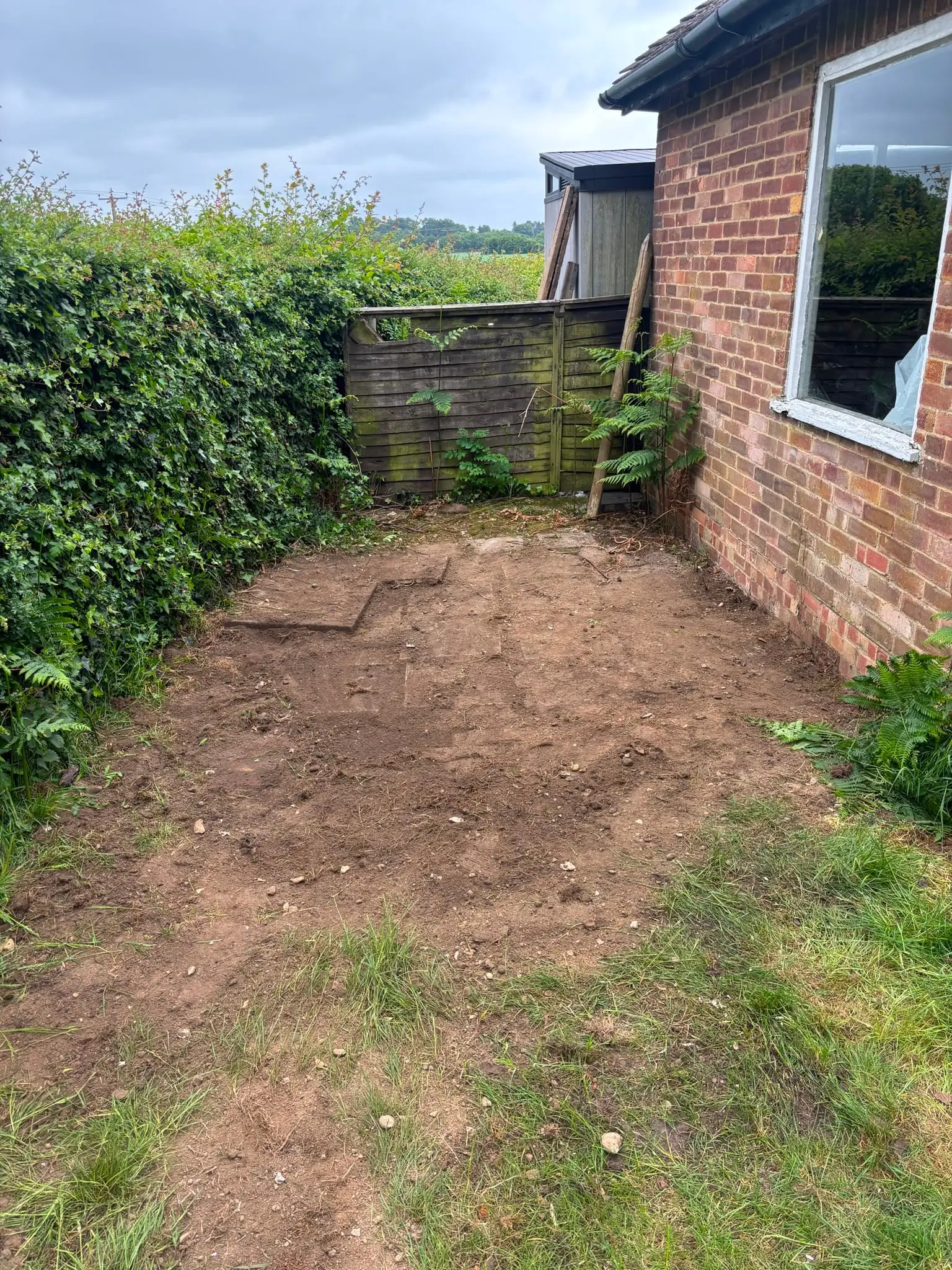 Cleared rear garden area beside a brick residential property.